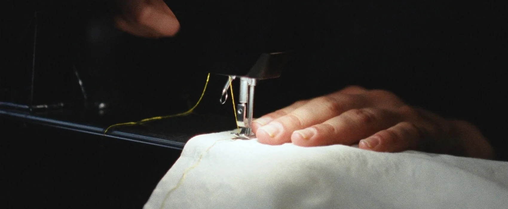 Hand guiding white fabric under a sewing machine needle threaded with gold